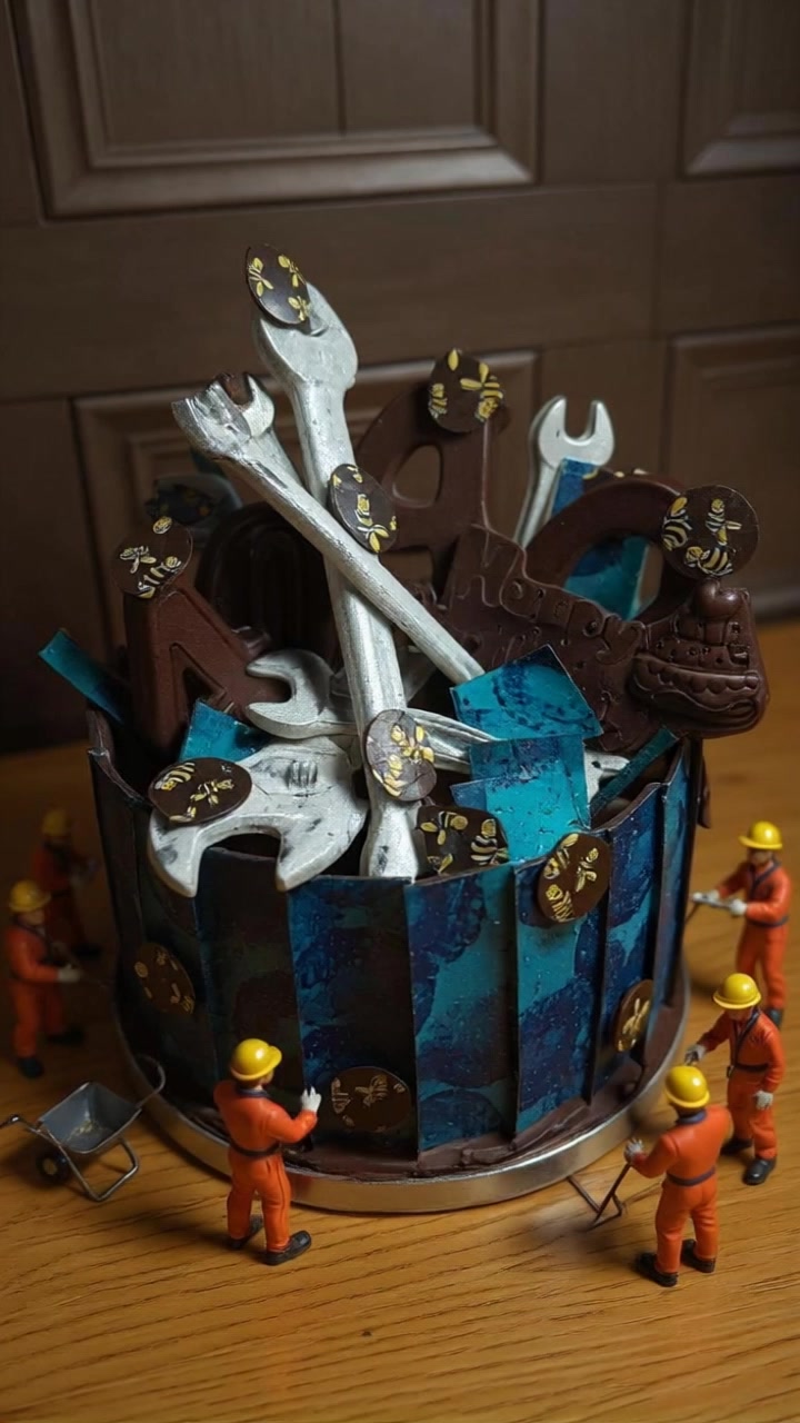 An elaborate chocolate celebration cake decorated with chocolate tools, bees and tiny construction figures